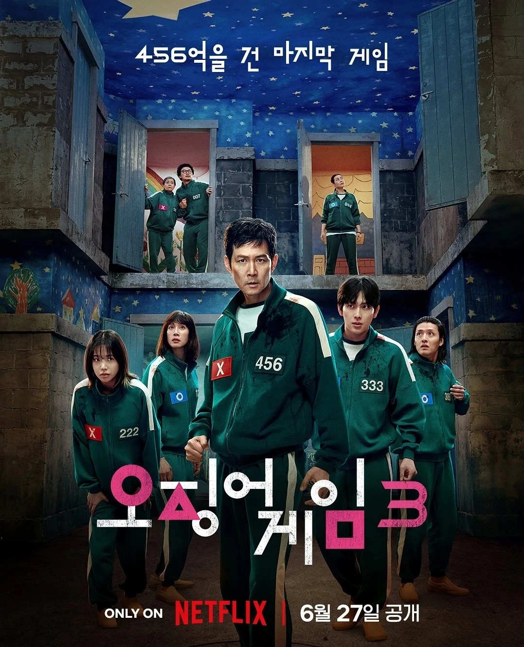 녹색 트레이닝복에 가슴에 번호를 단 다섯명의 게임 참가자들이 앞을 보며 서있고 뒤로는 2층에서 열려있는 두개의 문에 2명, 1명이 서서 앞을 바라보고 있다.